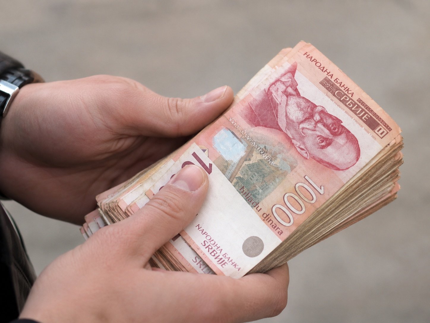 Ruke drže bunt novčanica od 1000 dinara.